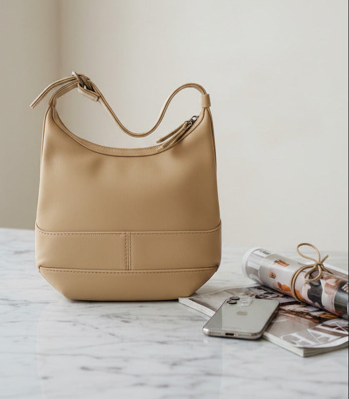 A beige faux-leather shoulder bag with a wide strap and a horizontal seam detail on the front, shown against a plain white background.