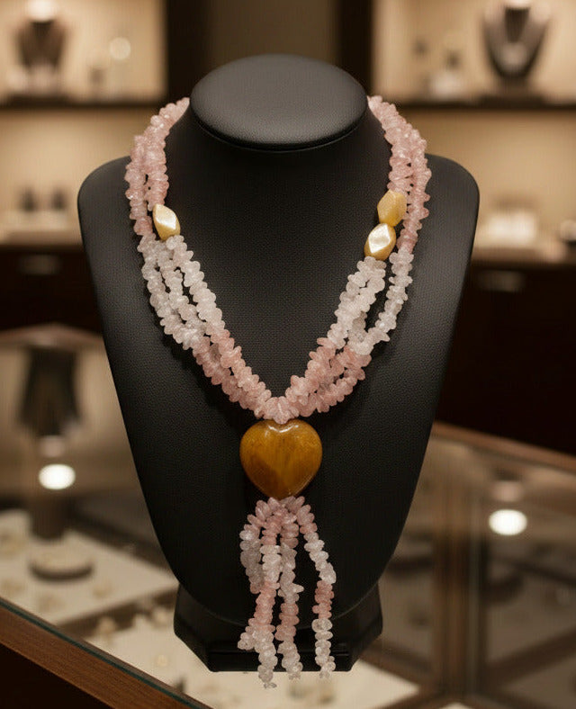 A crystal necklace featuring strands of light pink and white quartz chips with a polished amber heart-shaped bead and small faceted amber beads at the top, set against a plain white background.