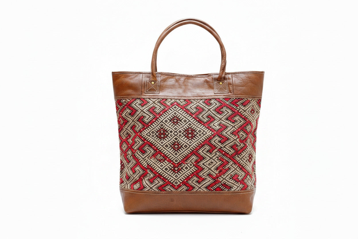 A woman holding a brown authentic leather handbag with a geometric berber style patterned front panel on a white background