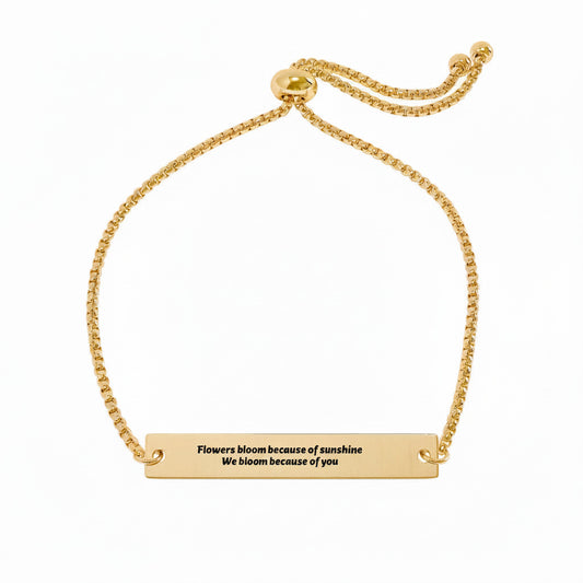 Gold bracelet with the text 'Flowers bloom because of sunshine. We bloom because of you' engraved on the bar charm--TTP