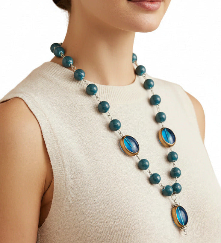 A beaded necklace featuring marbled teal blue beads and two large oval blue glass inserts with gold-toned metal trim, shown against a plain white background.
