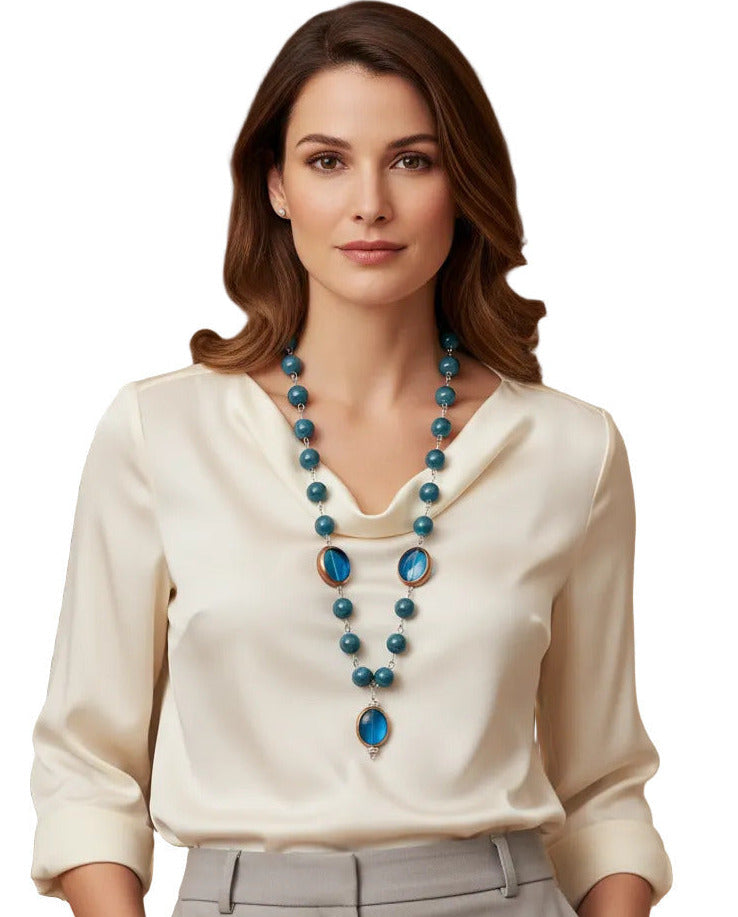 A beaded necklace featuring marbled teal blue beads and two large oval blue glass inserts with gold-toned metal trim, shown against a plain white background.