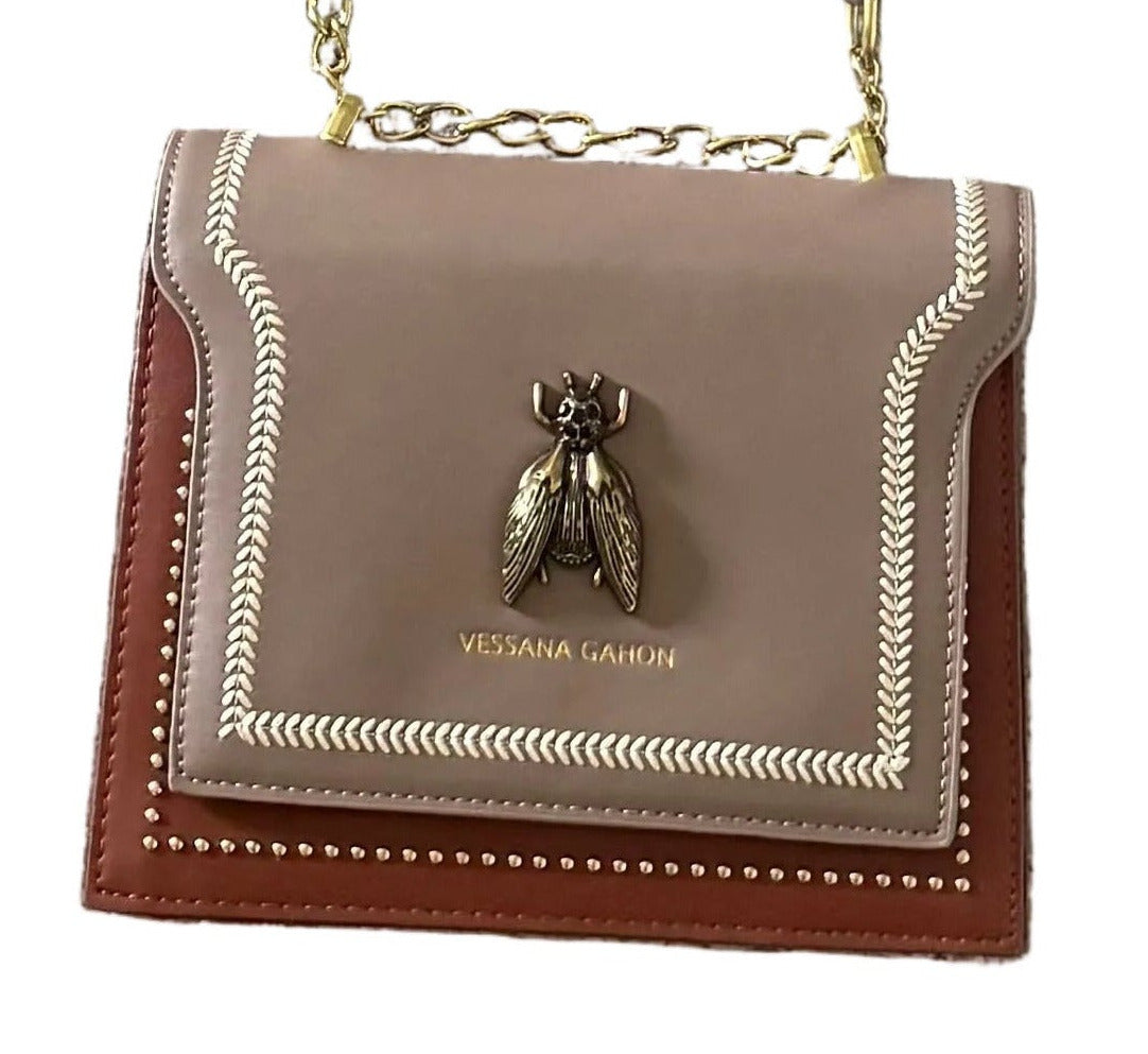 A small Vessana Gahon shoulder bag in taupe and brown leather with gold-tone chain strap and a bee hardware accent on the front flap, shown against a plain white background.