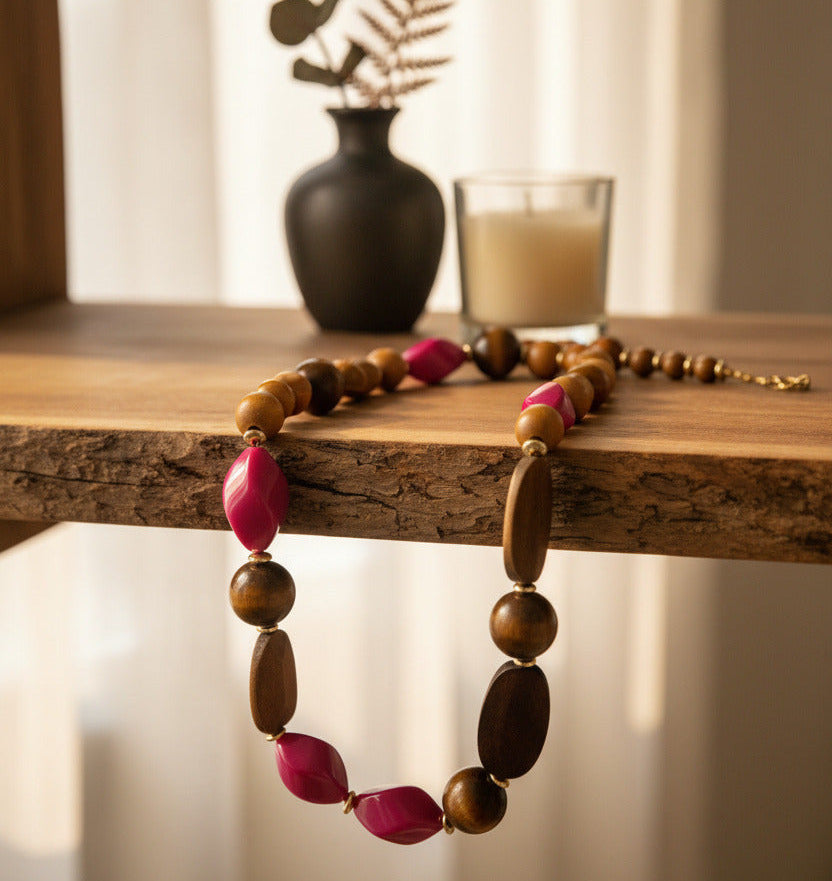 A beaded necklace featuring natural brown wood beads, faceted pink glass beads, and small gold spacer rings, displayed on a clean white background.