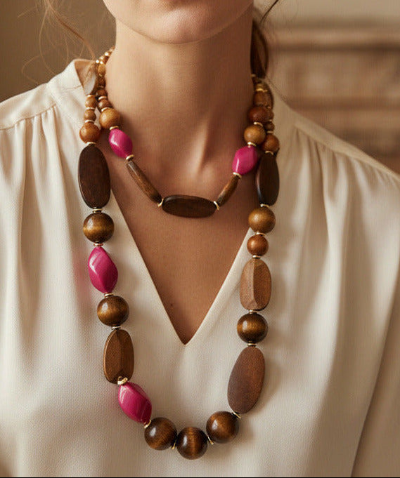 A beaded necklace featuring natural brown wood beads, faceted pink glass beads, and small gold spacer rings, displayed on a clean white background.