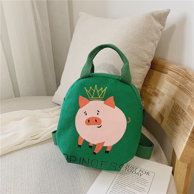 Green small round bag with the image of a pink pig on a surface with a pillow and wooden chair in the background.