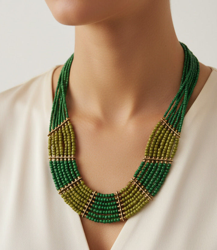 A multi-strand beaded statement necklace featuring shades of green and olive green beads accented with small gold spacer rings, displayed on a clean white background.