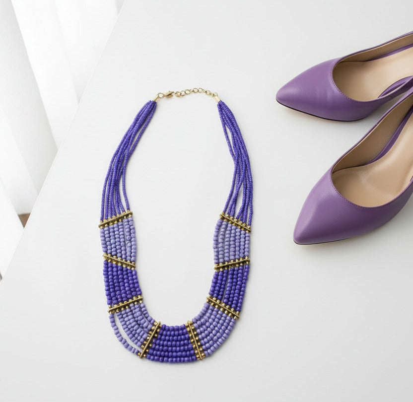 A multi-strand beaded necklace with a gradient of purple and light blue beads, accented by gold spacer rings and a gold clasp, shown on a plain white background.