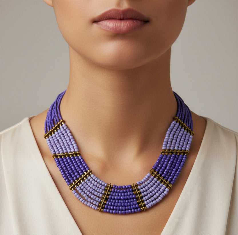 A multi-strand beaded necklace with a gradient of purple and light blue beads, accented by gold spacer rings and a gold clasp, shown on a plain white background.