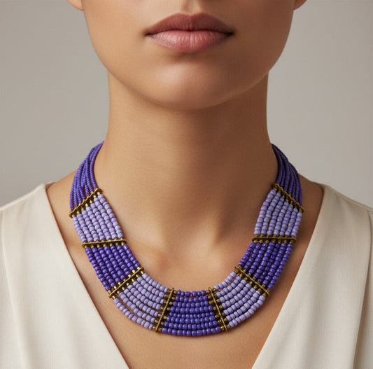 A multi-strand beaded necklace with a gradient of purple and light blue beads, accented by gold spacer rings and a gold clasp, shown on a plain white background.