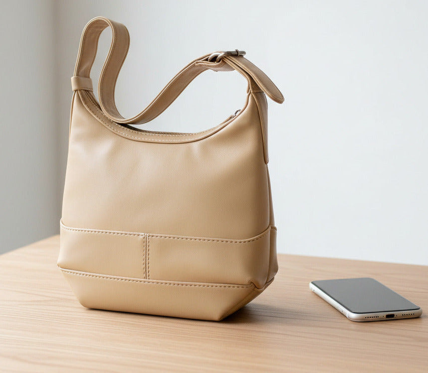 A beige faux-leather shoulder bag with a wide strap and a horizontal seam detail on the front, shown against a plain white background.