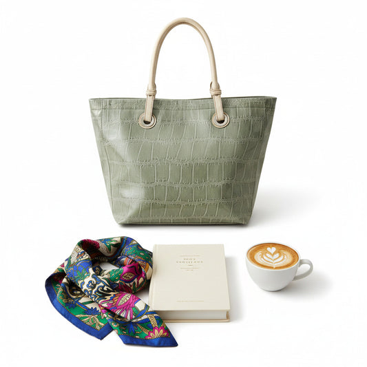 An gray crocodile-embossed leather tote bag with light beige shoulder straps and metal grommets, shown against a plain white background.