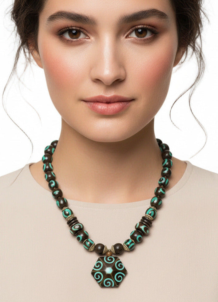 A beaded necklace featuring a large hexagonal pendant with turquoise and brown spiral patterns, flanked by dark brown and turquoise beads with metallic spacer details, shown against a plain white background.