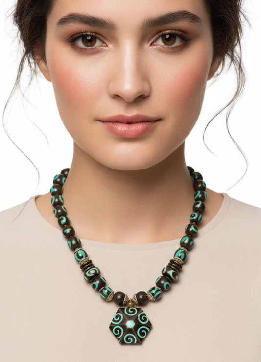 A beaded necklace featuring a large hexagonal pendant with turquoise and brown spiral patterns, flanked by dark brown and turquoise beads with metallic spacer details, shown against a plain white background.