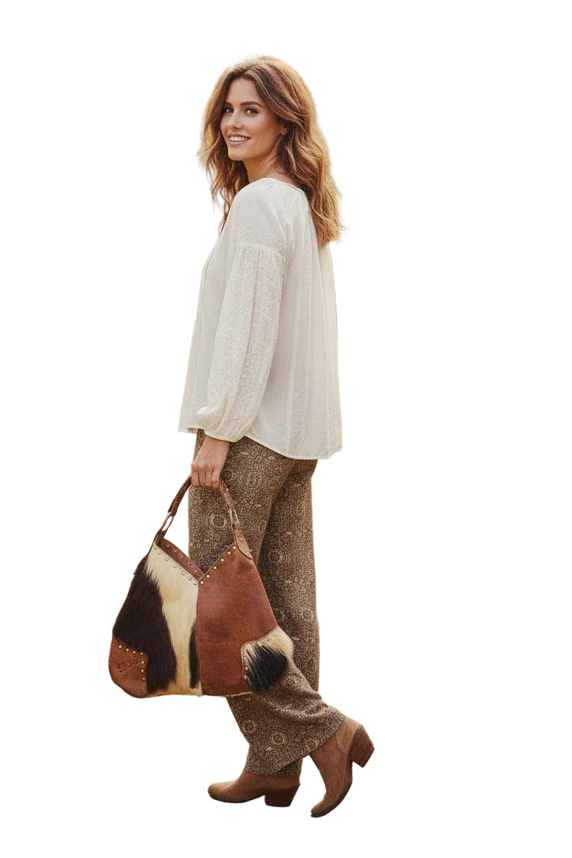 A brown genuine leather shoulder bag with metal studs, and a wide adjustable strap, isolated on a white background.