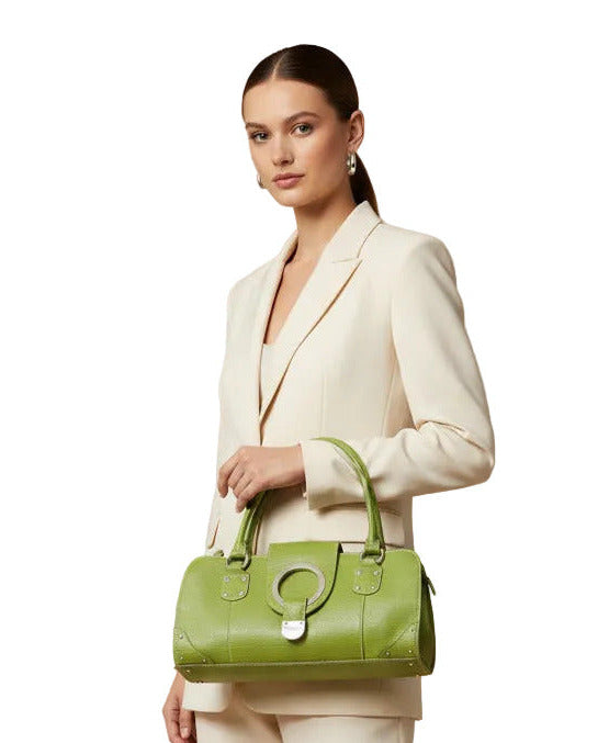 A woman carrying a lime green textured leather handbag with a large silver-tone circular ring detail on the front flap, silver studs, and a top handle, shown against a plain white background.