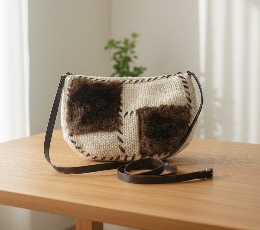 A handmade shoulder bag featuring a cream-colored knit body with two dark brown faux fur panels and a black leather strap, set against a plain white background.