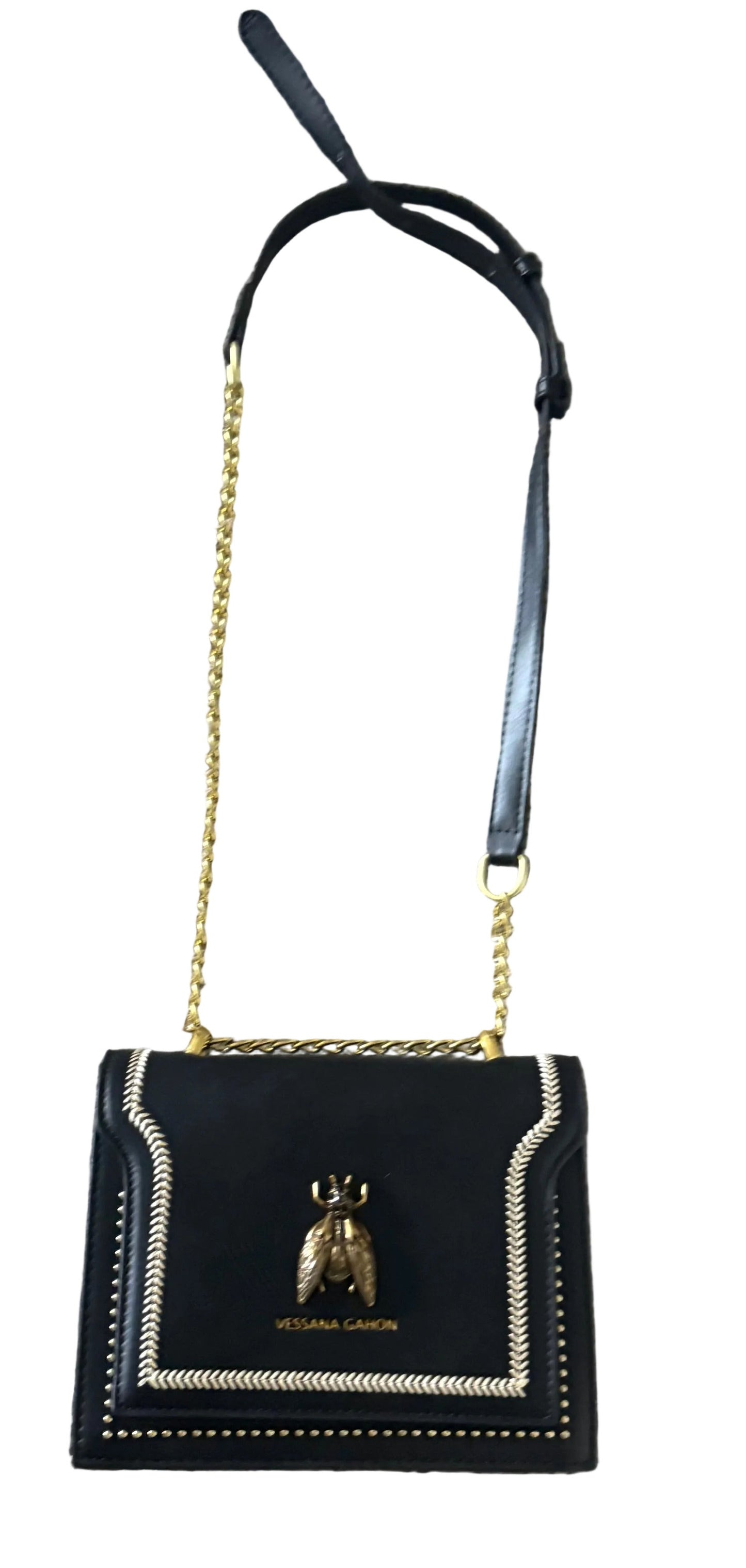 A black Vessana Gahon crossbody bag with a gold chain strap, an adjustable black leather shoulder strap, and a gold bee logo clasp on a gray carpeted floor.
