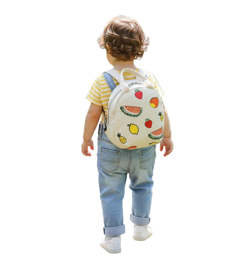 A kid carrying a cream small round bag with fruit patterns on a white surface.