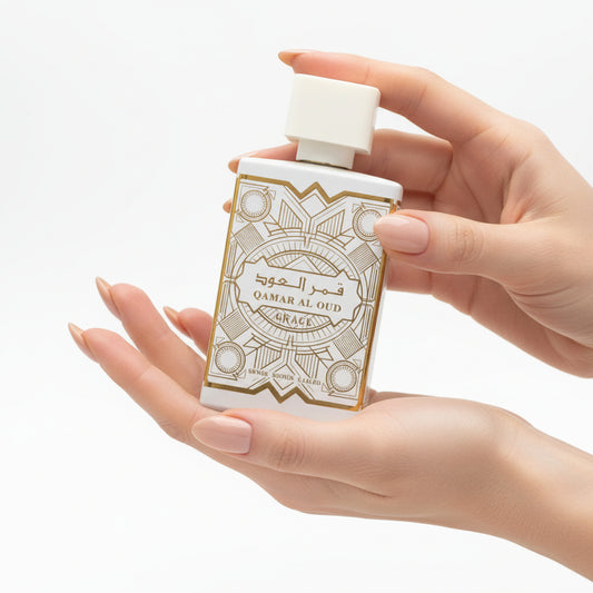 A hand holding a bottle of Qamar Al Oud Grace perfume displayed A bottle and box of Qamar Al Oud Grace perfume displayed against a white background.