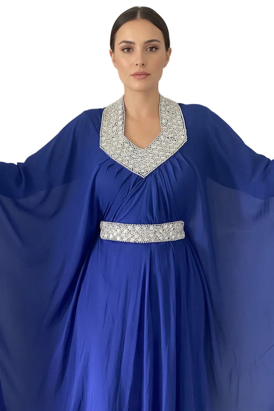 Woman wearing a blue dress with a silver embellished neckline and waistband against a plain background