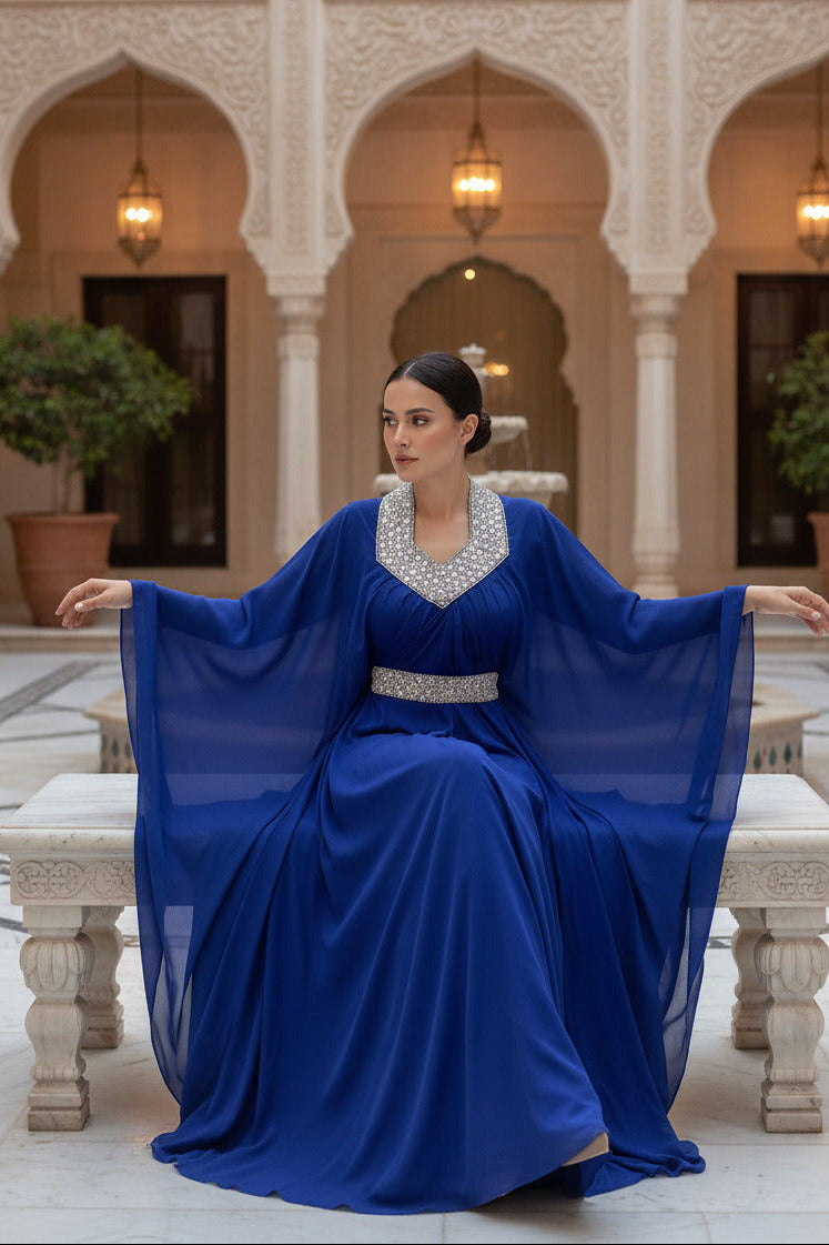Woman wearing a blue dress with a silver embellished neckline and waistband on a white background