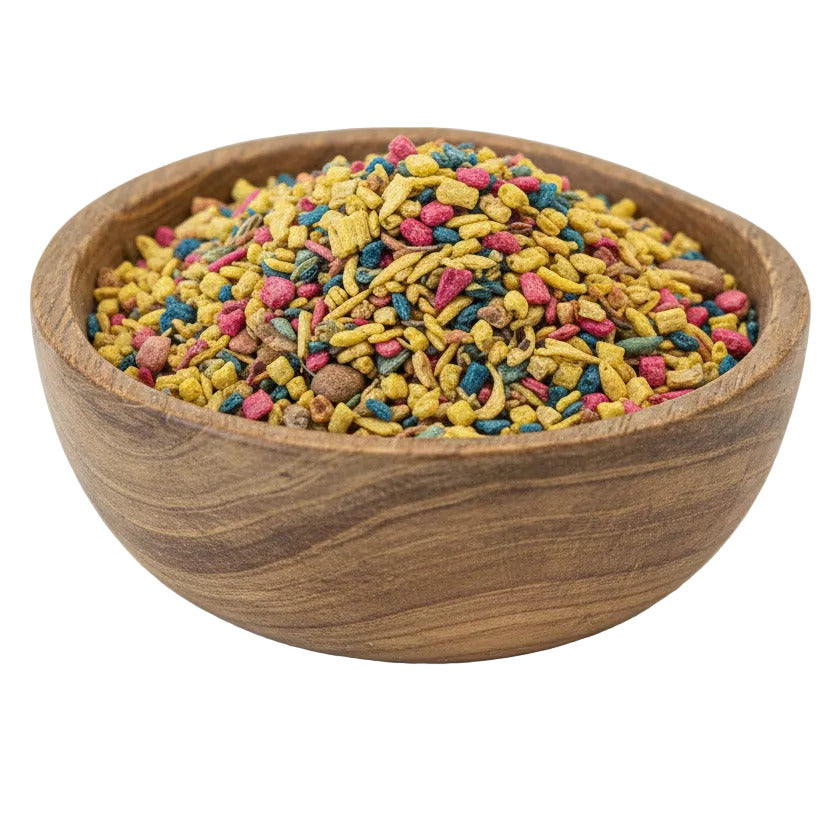 A wooden bowl filled with multicolored dry pet food pieces, including yellow, green, red, and brown pieces, photographed on a plain white background.