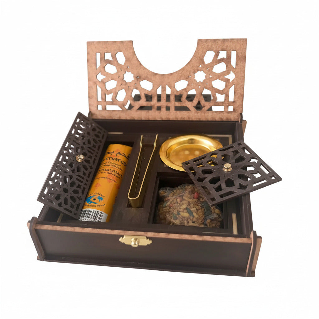 An open wooden incense box with geometric cutout details, containing a  tube of Charcoal incense, a gold metal tong, a small round burning dish, and a clear compartment with dried Serghina incense, set on a white background--TTP
