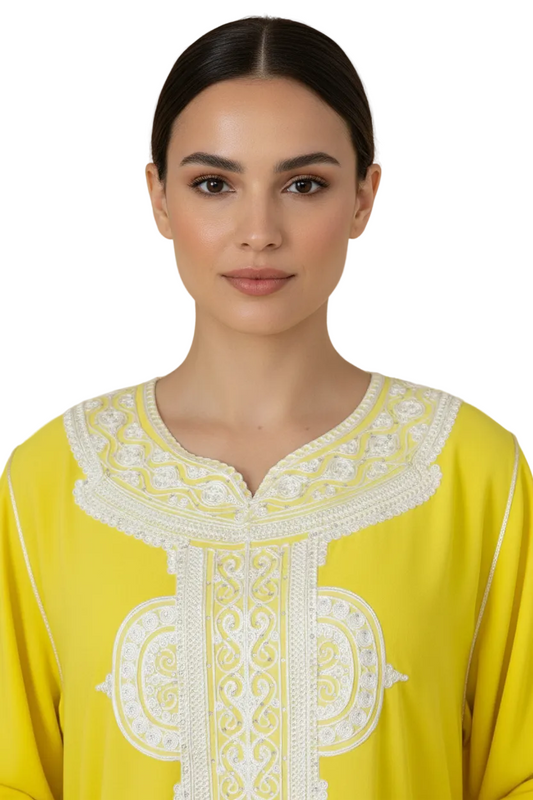 Woman wearing a yellow dress with intricate white embroidery against a beige background